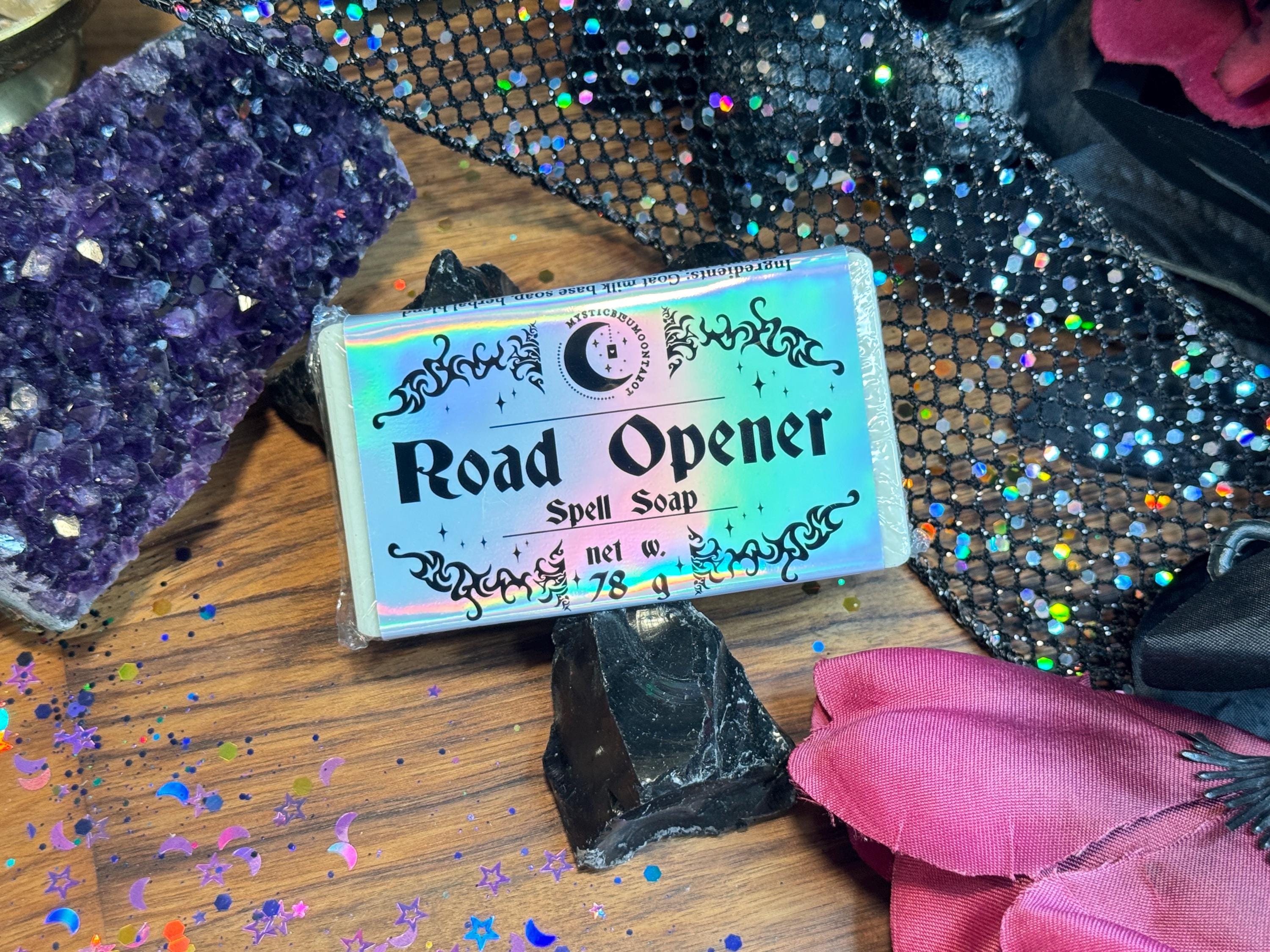 May include: A holographic bar of soap with the text "Road Opener Spell Soap" and "net w. 78 g". The soap is on a wooden surface with glitter and a purple amethyst crystal.